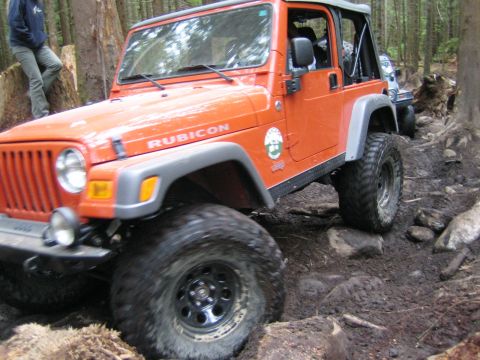 1990 Ford Bronco - This Jeep Wrangler Rubicon is navigating a challenging off-road trail with large rocks and mud.