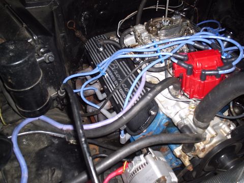 1985 Ford Bronco - Overhead shot into an engine bay showing a blue Ford V8 with finned aluminum valve covers reading "Powered by Ford," a red HEI-style distri…