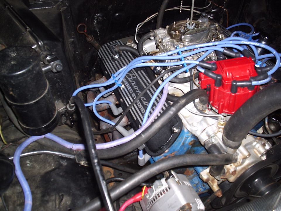 Ford V8 with finned valve covers, red distributor cap and blue plug wires in engine bay