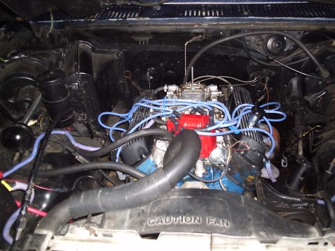 1985 Ford Bronco - Overhead engine bay view of a blue-block V8 with finned aluminum valve covers, an exposed four-barrel carburetor with no air cleaner, and b…