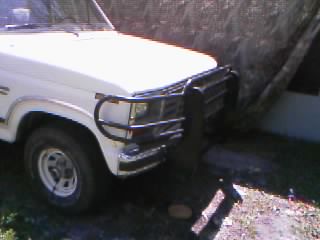 1986 Ford Bronco - A white Ford truck is parked outdoors, partially covered by a tarp.