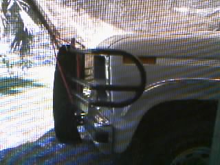 1986 Ford Bronco - Grainy close-up of the front corner of a white Ford truck fitted with a black tube brush guard wrapping around the headlight area, with bum…