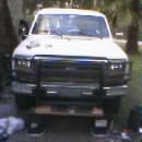 1986 Ford Bronco - Very small, low-resolution head-on front view of a white 1980s Ford truck or Bronco fitted with a black tube brush guard over the grille an…
