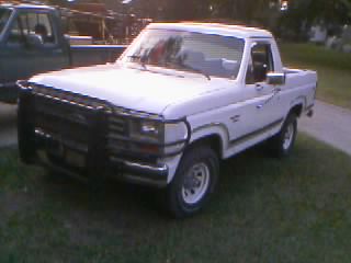 1986 Ford Bronco - Small low-resolution three-quarter front shot of a white 1980s Ford Bronco with the rear top removed, wearing a black tube brush guard, chr…