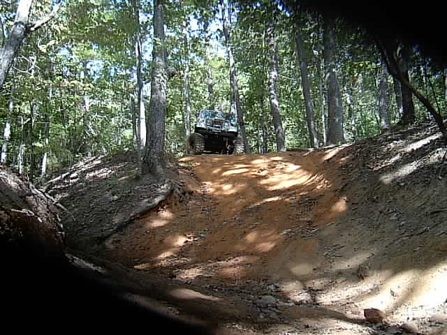 Jeep Wrangler topping a steep orange-dirt climb among tall trees
