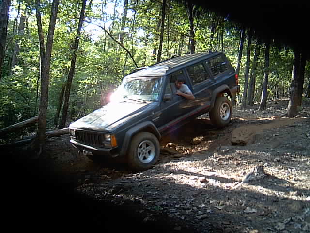 Dark Jeep Cherokee XJ tipped on an off-camber dirt trail, driver leaning out window