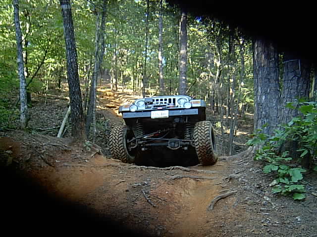 Front of a lifted Jeep with light bar dropping into a deep wooded mud rut