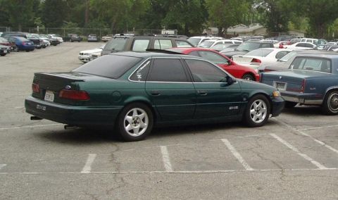 1993 Ford Taurus - A dark green 1993 Ford Taurus sedan is parked in a lot with other vehicles.
