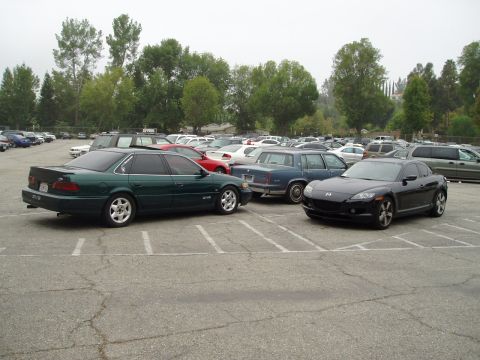 1993 Ford Taurus - A green 1993 Ford Taurus and a black Mazda RX-8 are parked in a lot with other vehicles.