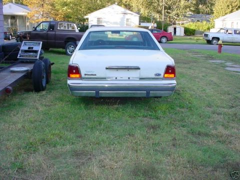 1991 Ford LTD Crown Victoria - A white 1991 Ford Crown Victoria is parked on a grassy lawn next to a trailer with tires.