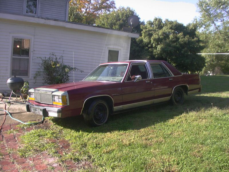Dark red Ford LTD Crown Victoria sedan on black steel wheels parked beside a white house