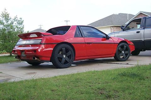 1988 Pontiac Fiero - Red 1988 Pontiac Fiero coupe with custom black wheels is parked next to a pickup truck.