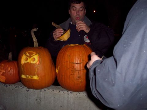 2001 Ford Crown Victoria - People are carving pumpkins at night, one with an owl design and another with a face.