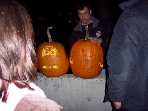 2001 Ford Crown Victoria - Two carved pumpkins, one an owl and the other a face, are displayed during a nighttime event.