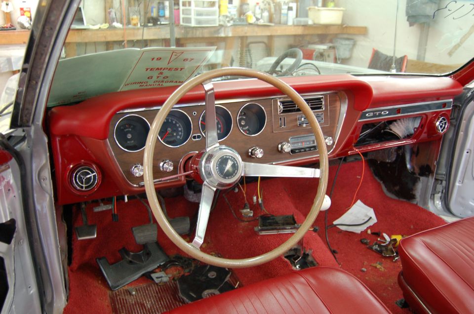 Red 1967 Pontiac GTO interior under restoration with woodgrain dash and GTO badge