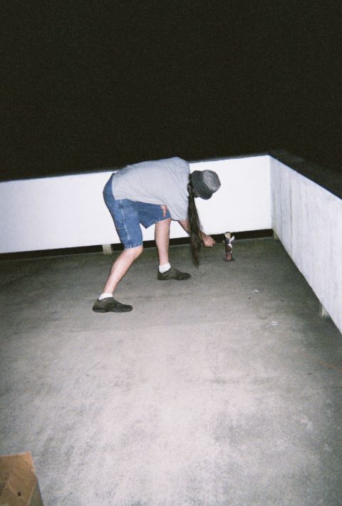 1990 Ford Bronco - A person in shorts and a hat bends down to retrieve a small figurine from a concrete area at night.