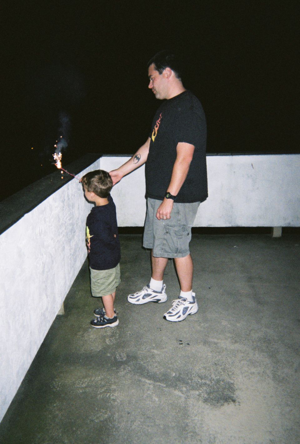 Dad holds a sparkler for his son to watch on a dark night