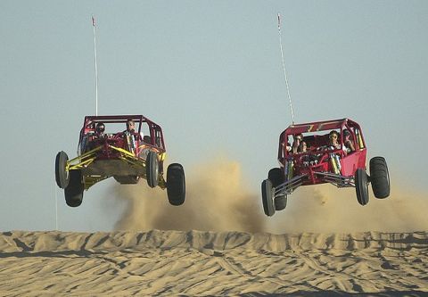 1978 Ford Bronco - Two dune buggies catch air while traversing sand dunes, kicking up dust.