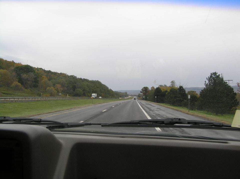 View through a windshield over a gray dash onto a divided highway in fall