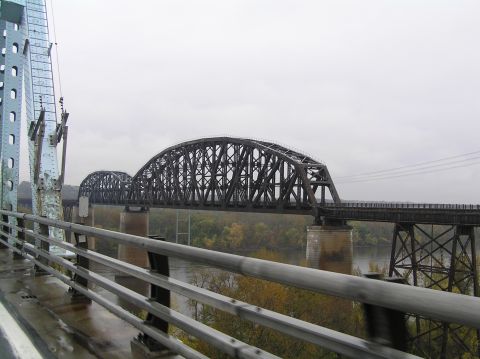 1997 Subaru Impreza - A view from a bridge shows a large steel truss railway bridge spanning a river on an overcast day.