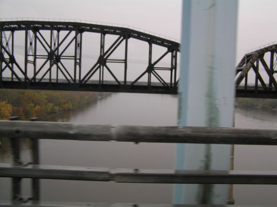 Metal truss bridge over a misty river with autumn trees on the bank