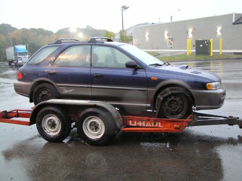 1997 Subaru Impreza - A blue 1997 Subaru Impreza wagon is loaded onto a U-Haul trailer on a wet day.