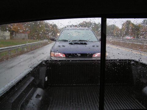 1997 Subaru Impreza - A blue 1997 Subaru Impreza is seen from behind on a rainy day, driving on the highway.