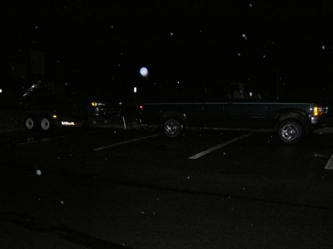 1997 Subaru Impreza - A dark pickup truck tows a U-Haul trailer in a parking lot at night, with visible precipitation in the air.