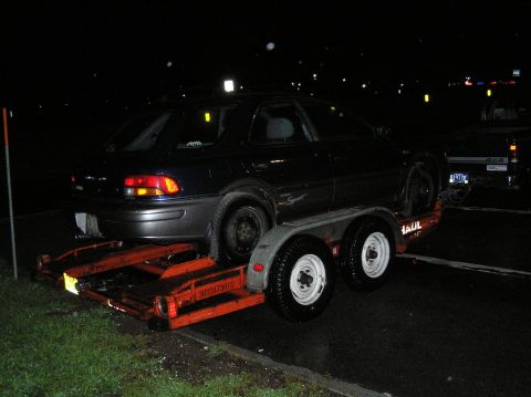 1997 Subaru Impreza - A dark sedan is loaded onto a trailer at night, with another vehicle visible in the background.