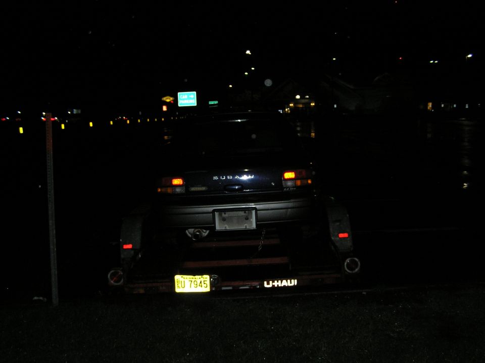 Rear of a dark Subaru Impreza wagon loaded on a U-Haul car trailer at night