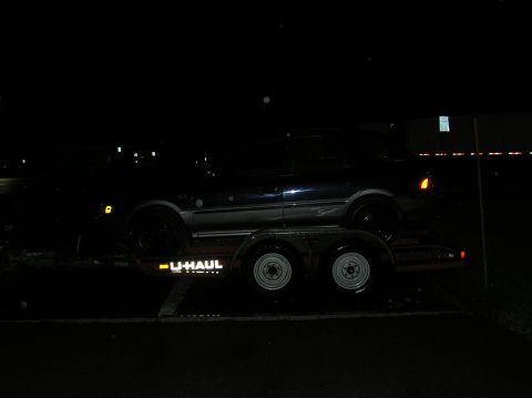 1997 Subaru Impreza - A dark sedan is transported on a U-Haul trailer at night, with visible U-Haul branding on the trailer.