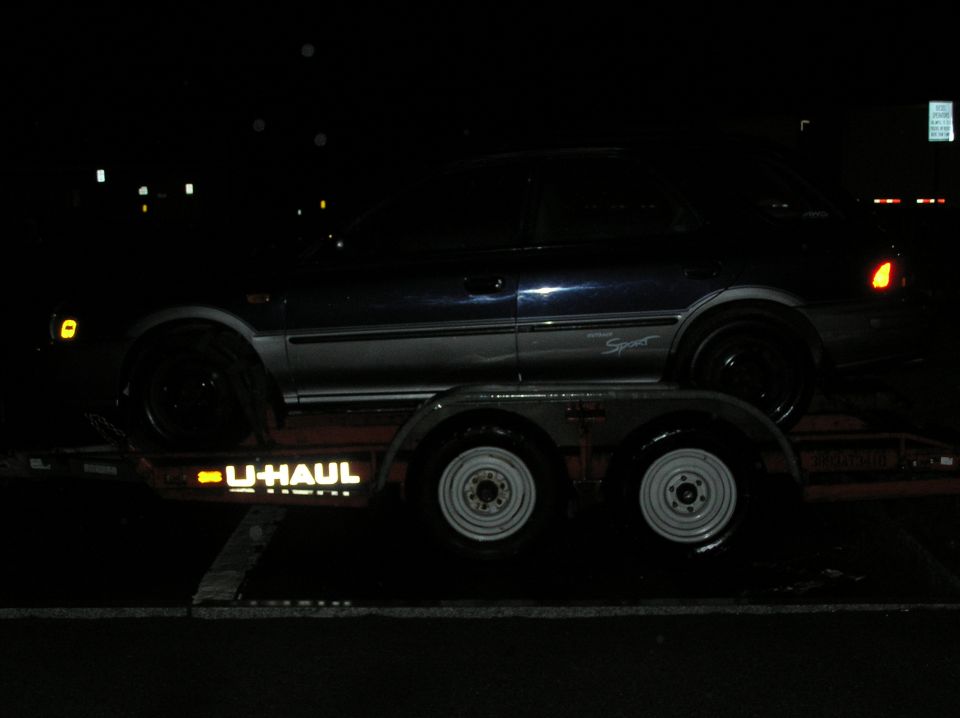 1997 Subaru Impreza on a U-Haul trailer at night, side view