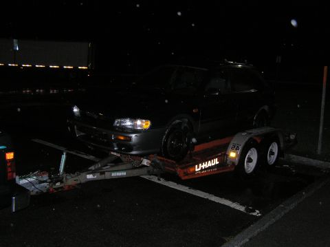1997 Subaru Impreza - A dark Subaru Impreza wagon is loaded onto a U-Haul trailer at night, with rain falling.