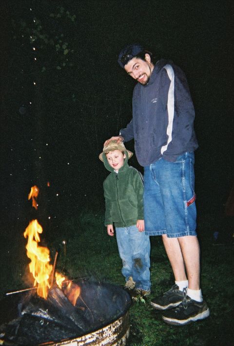 1990 Ford Bronco - A man and a child observe a campfire, with sparks rising into the dark sky.