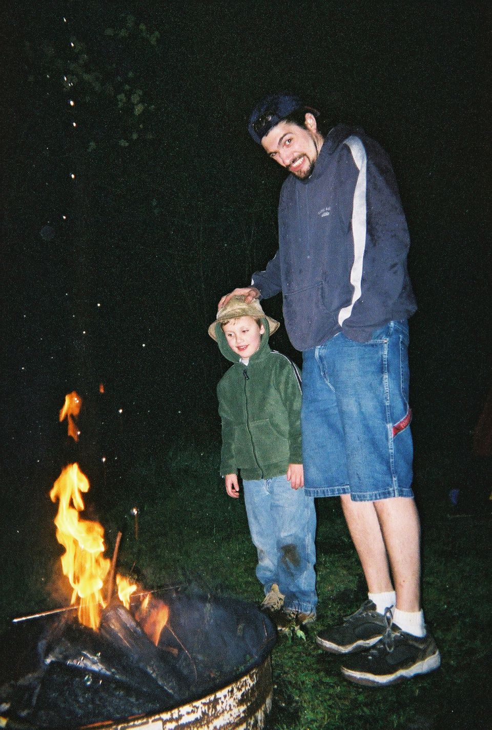 Two people stand by a campfire at night