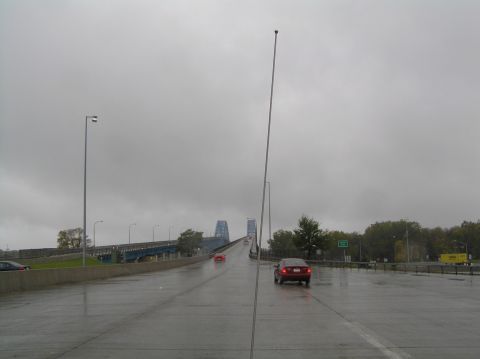 1997 Subaru Impreza - Vehicles travel across a wet bridge on an overcast day, with a large blue bridge in the background.