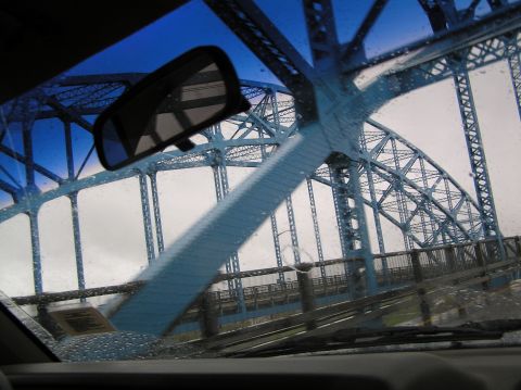 1997 Subaru Impreza - Driving across a blue truss bridge, seen through a rain-streaked windshield.