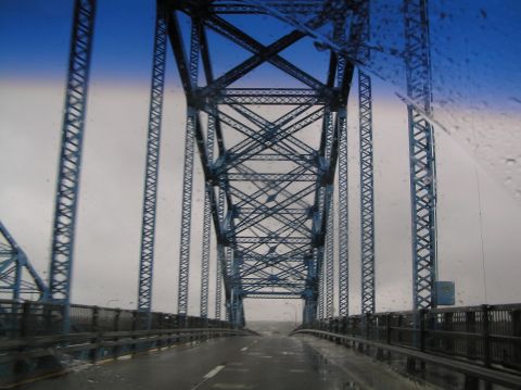 1997 Subaru Impreza - Driving over a large blue metal truss bridge with rain on the windshield.