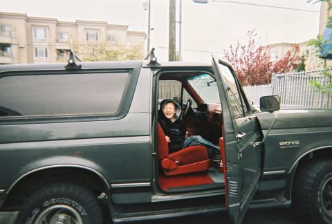 1990 Ford Bronco - Side view of a dark green full-size Ford Bronco with the passenger door open, showing a bright red vinyl interior with red bucket seat and…