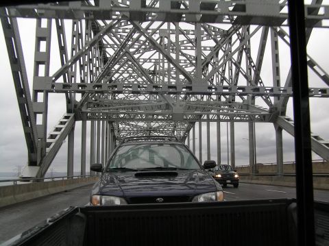 1997 Subaru Impreza - A dark blue Subaru Impreza drives across a large metal bridge under a cloudy sky.