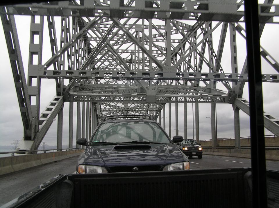 Dark blue Subaru Impreza with hood scoop following a truck across a steel truss bridge