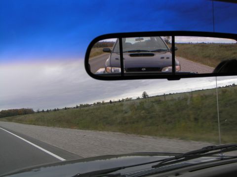 1997 Subaru Impreza - A dark 1997 Subaru Impreza is visible in the rearview mirror as the camera car travels down a highway.