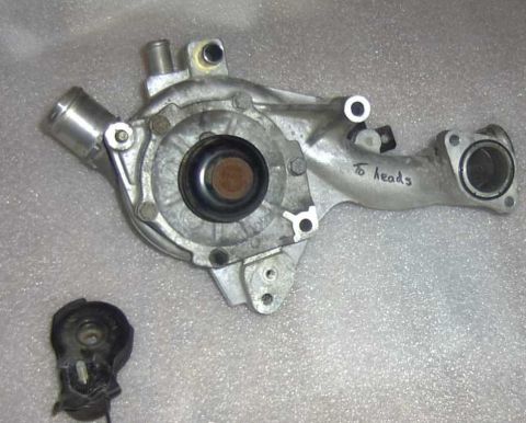 1997 Ford Taurus - A metal water pump is shown with a separate black component. Text handwritten on the pump reads "to heads".