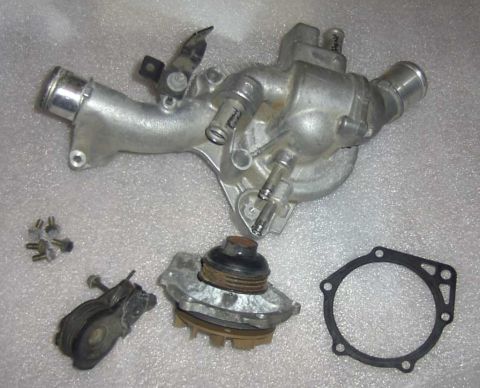 1997 Ford Taurus - A water pump laid out disassembled on a gray countertop: the cast aluminum housing with integral coolant crossover tube and hose necks at t…