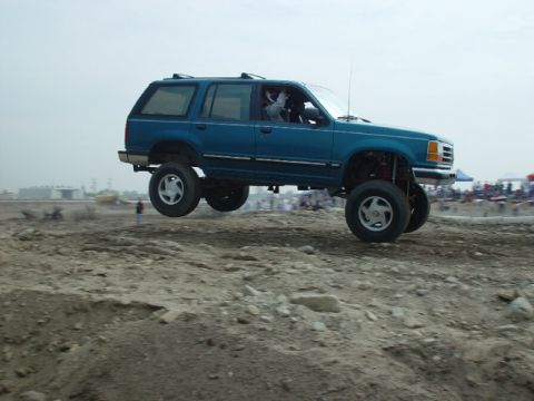 1984 Ford Bronco - A lifted blue SUV with off-road tires catches air during an off-road event.