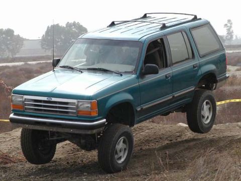 1984 Ford Bronco - This teal Ford Explorer is shown navigating rough terrain with its front wheels off the ground.
