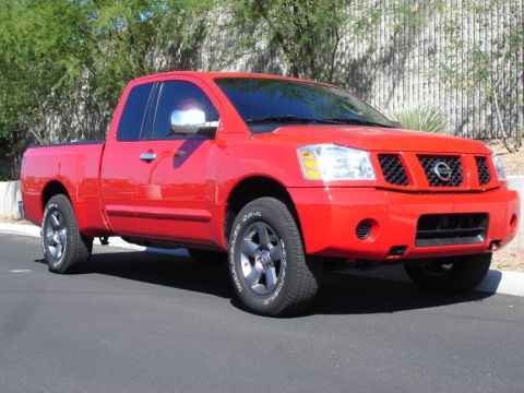 2005 Nissan Titan - A red pickup truck is parked on a street with trees in the background.
