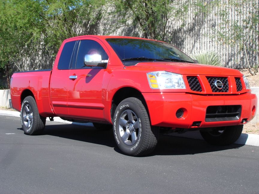 Red Nissan Titan king cab with body-color bumper, front 3/4 passenger side