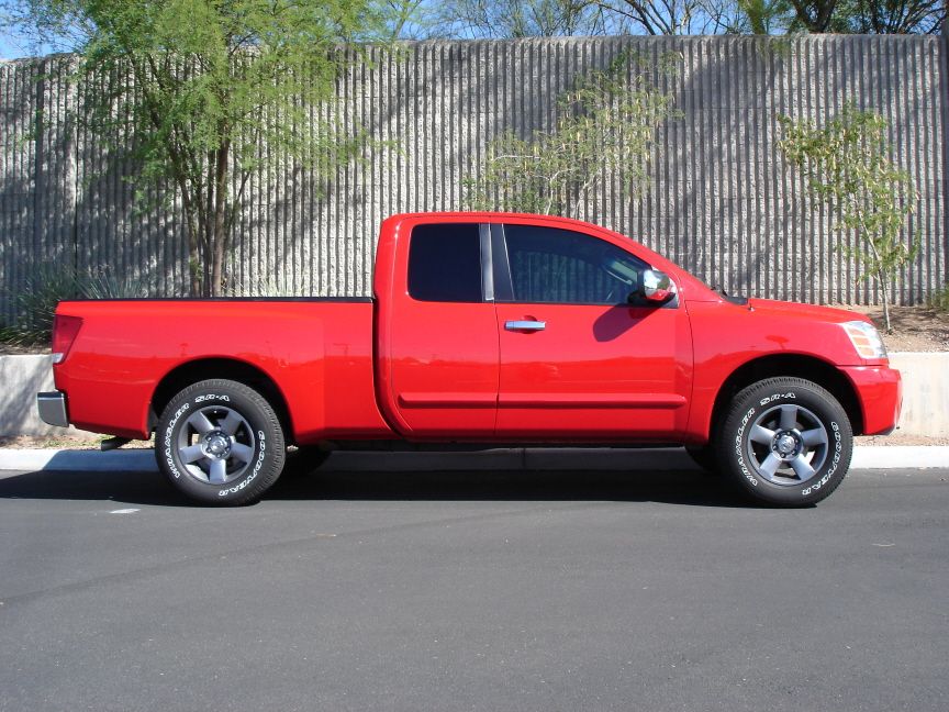 Red Nissan Titan king cab pickup, full side profile parked by a block wall