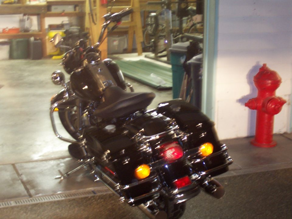 Black touring motorcycle with saddlebags and tall handlebars parked in a garage next to a red fire hydrant